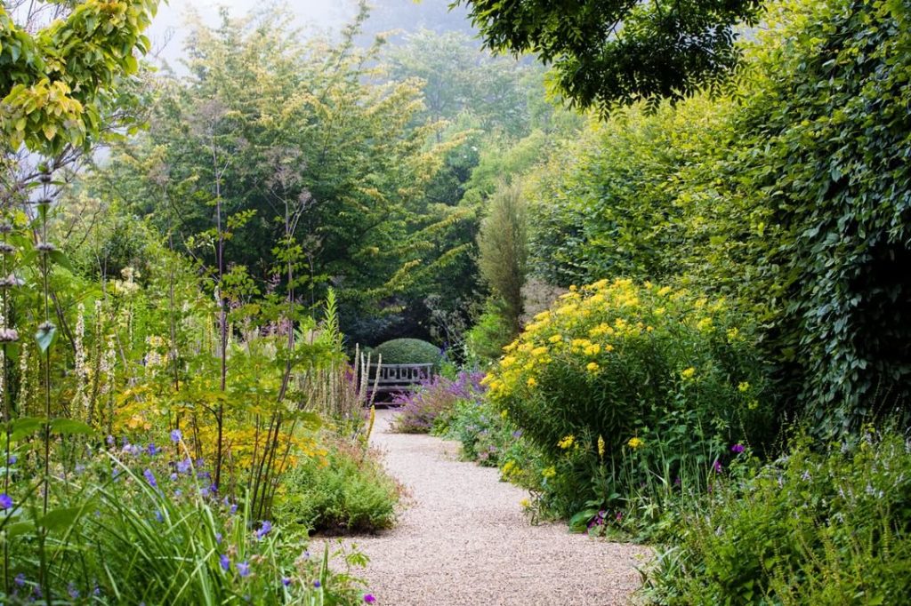 @gardendesignmag: A wood bench backed by a clipped globe of bush germander draws the eye along a g…