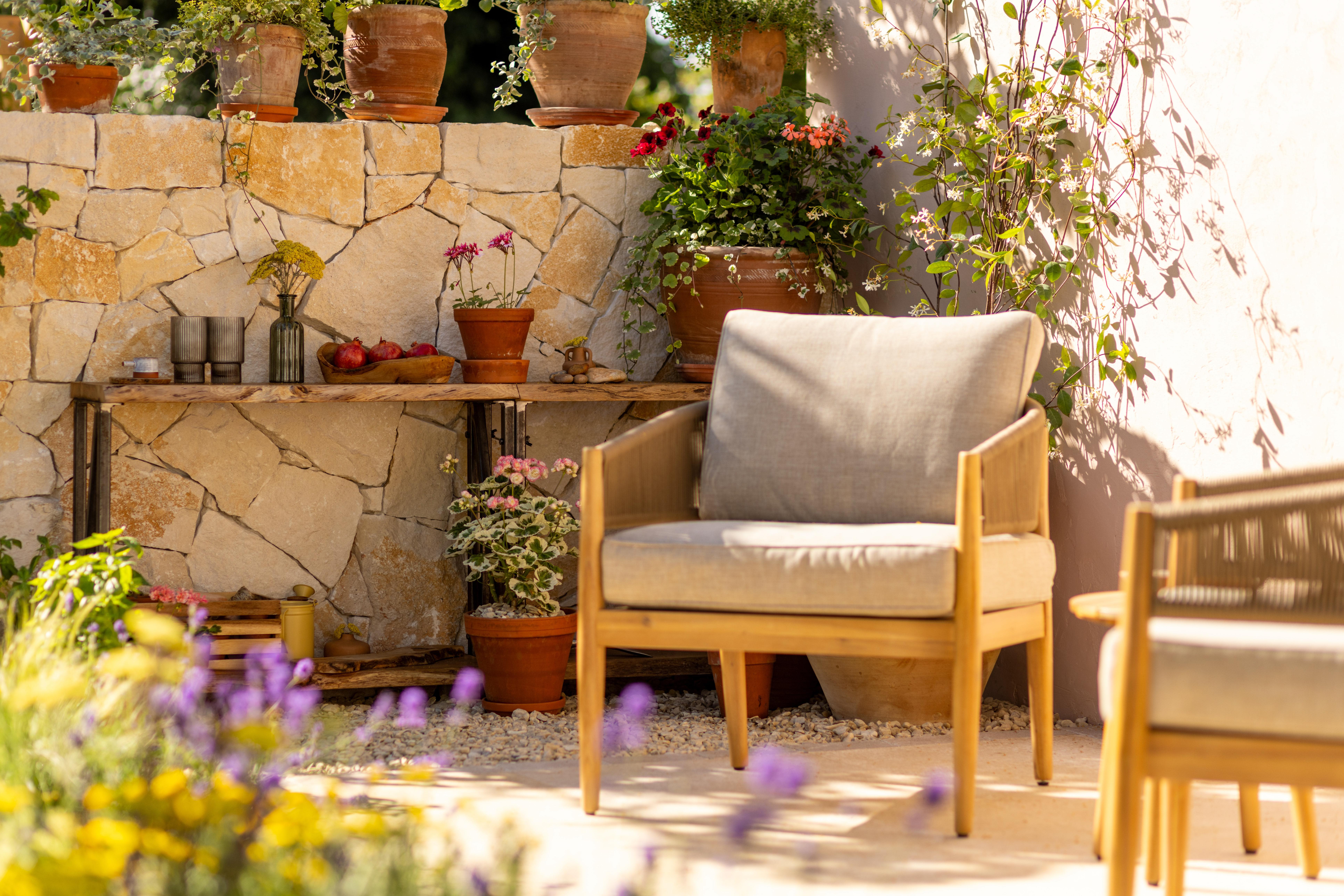 Outdoor patio furniture and potted plants against a stone wall.