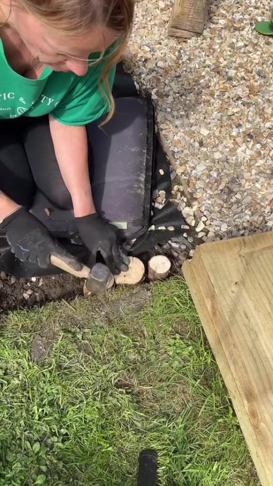 Person using a hammer to install wood slices in a garden.