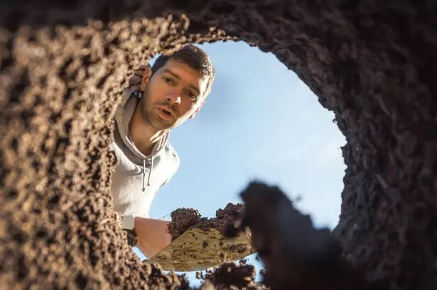 A young guy digging a deep hole with a shovel is surprised by an amazing find. View from the underground at the grave digger.