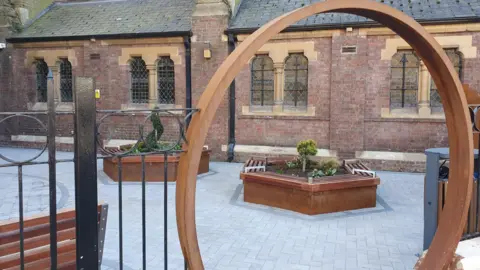 East Midlands Sexual Health/HTL Church Wooden arch, revealing a garden in front of a church with planted raised beds