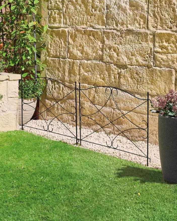 Black metal garden fence against a stone wall.