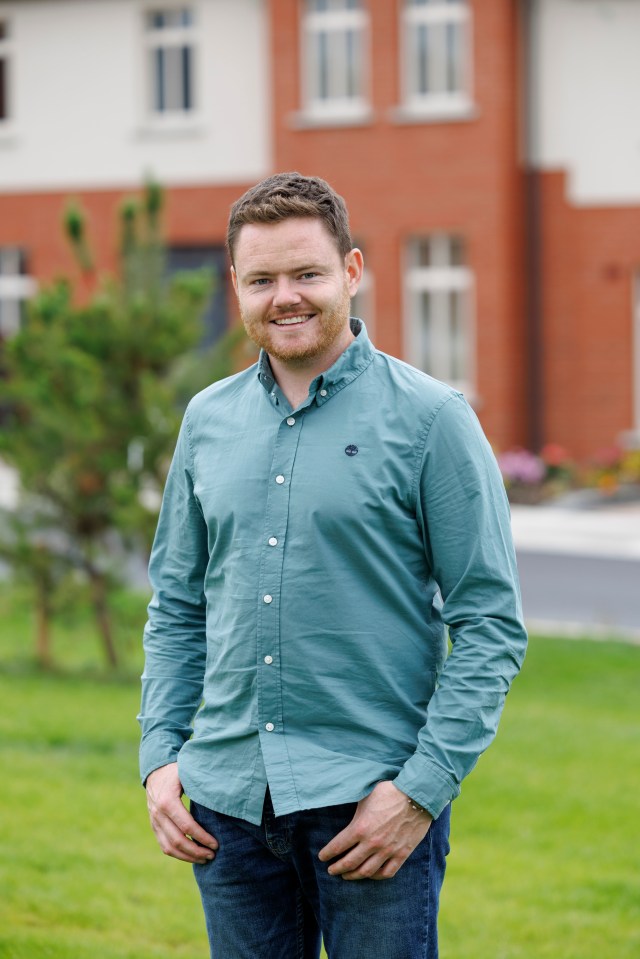 Man smiling outdoors in front of a house.