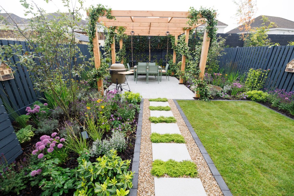 Supergarden 2024: A paved patio with a wooden pergola, outdoor dining set, and a meticulously landscaped garden.