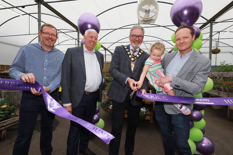Four men and a baby cutting a ribbon inside a new garden centre