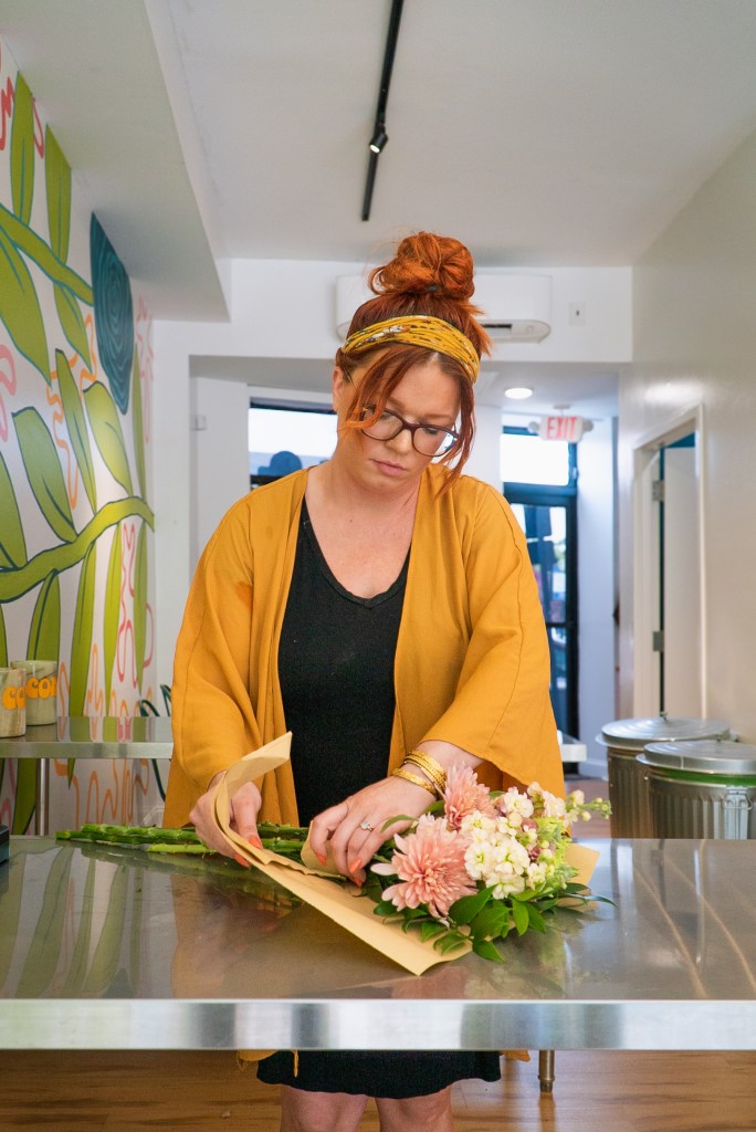A woman wearing a yellow cradigan looks down as she wraps a bouquet