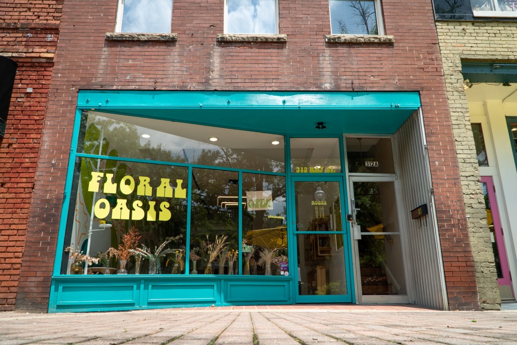 A glass storefront with teal trim, showing the Floral Oasis logo on the window