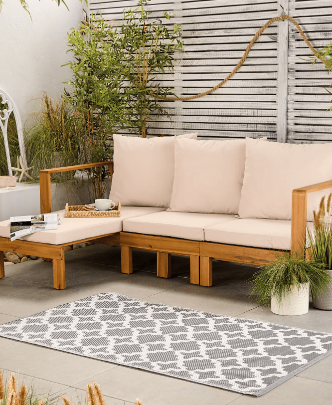 Grey and white patterned outdoor rug in front of a wooden patio sofa.