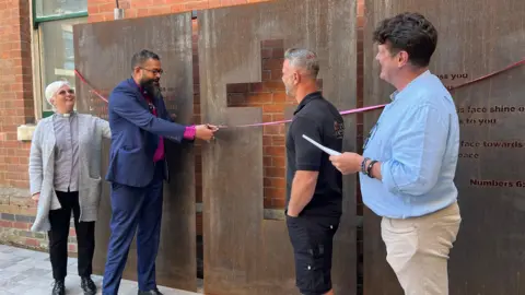 BBC Bishop Saju, cuts the ribbon alongside the Vicar of Holy Trinity Church, Elaine Sutherland, and Alistair Hudson, the former CEO of East Midlands Sexual Health formerly known as LASS.   