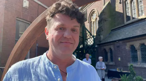 Alistair Hudson, wearing a blue shirt in front of the new garden.