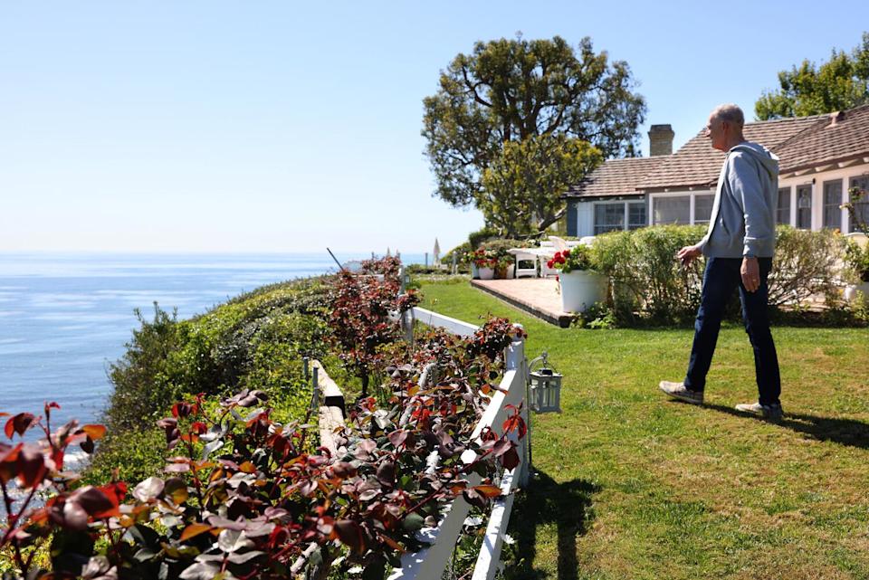 A tall, slender man, Dan Bifano, striding on a green lawn near the edge of a cliff overlooking the ocean.