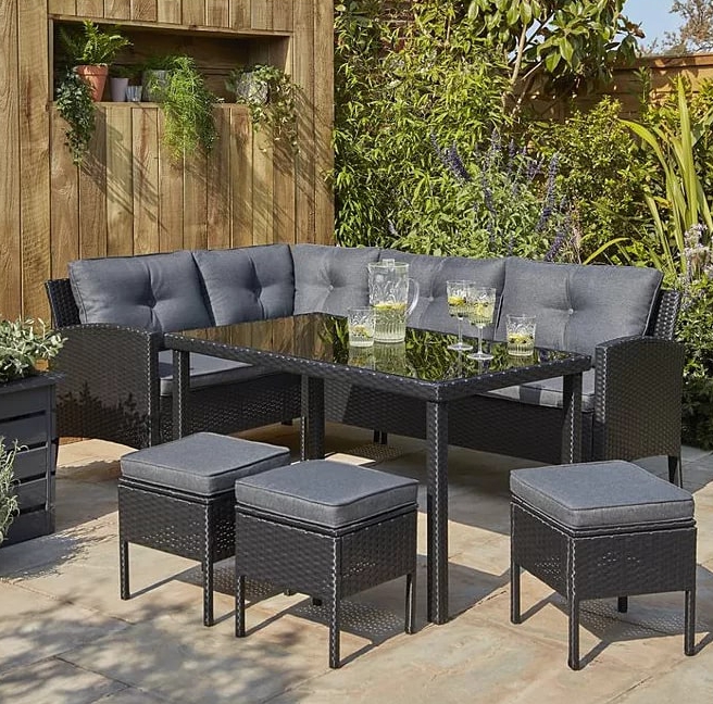 Black rattan outdoor corner sofa dining set with table and stools.