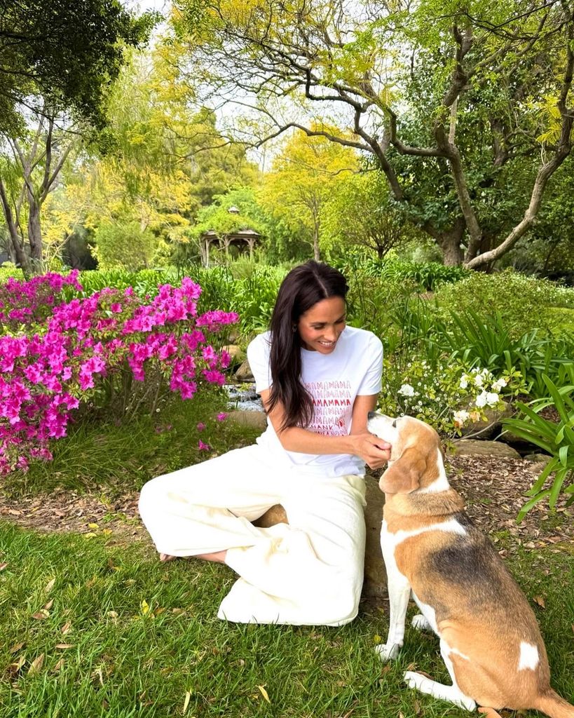 A photo of Meghan Markle wearing cream and sitting in her colourful garden with her dog Mia 