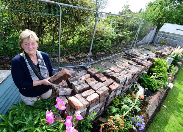 Linda Hufton with bricks in her garden,after a wall collapsed from the bowling club at the back of her West Derby house