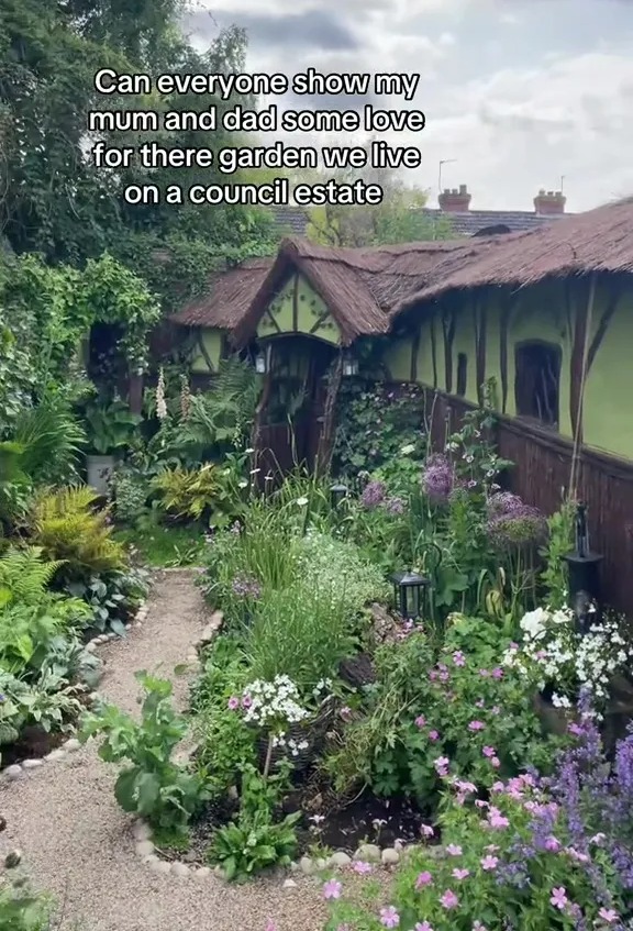 A lush garden with a whimsical cottage-like structure, situated on a council estate.