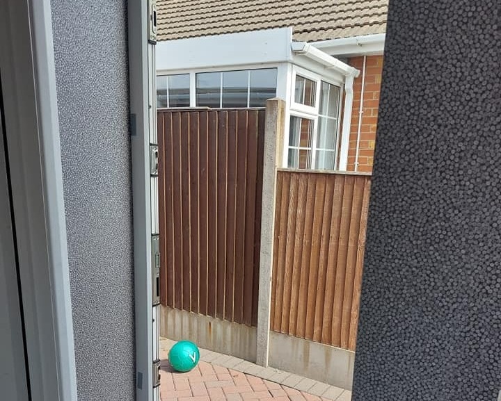 View through a door showing a backyard with a ball and shoes.