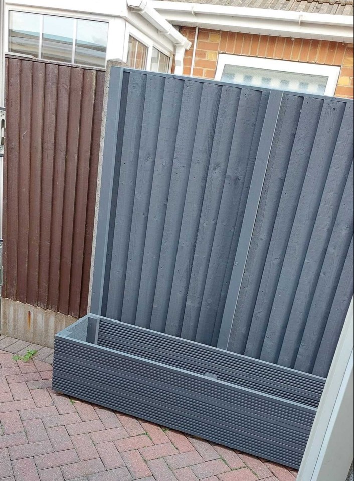 A gray planter and a gray fence section in a brick paved backyard.