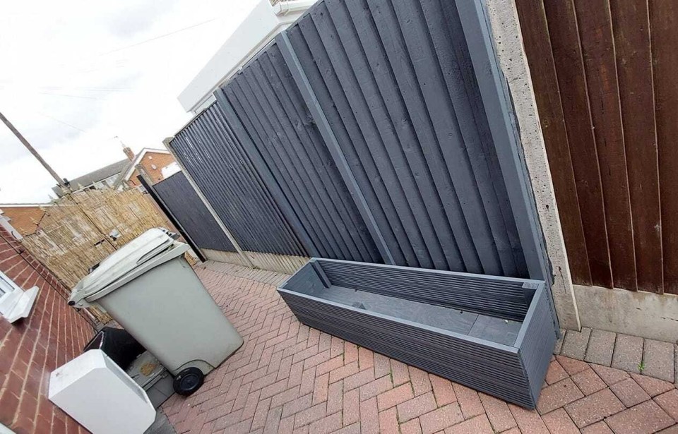 Grey planter in a backyard between two fences.