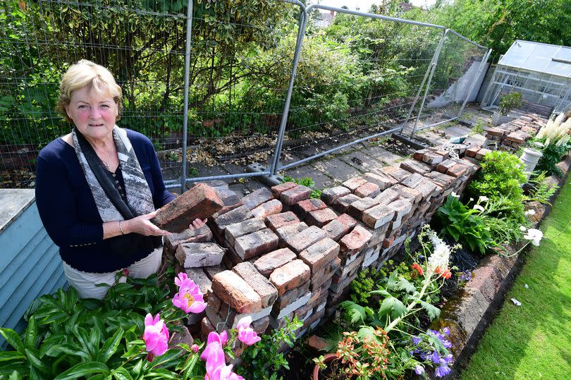 Linda Hufton with bricks in her garden,after a wall collapsed from the bowling club at the back of her West Derby house