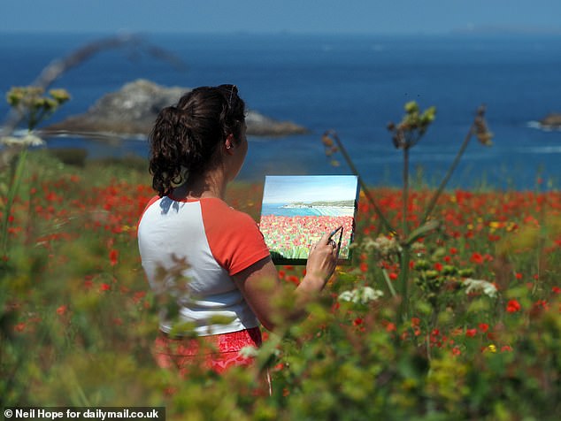 A person stands by the poppies painting the stunning scene around her