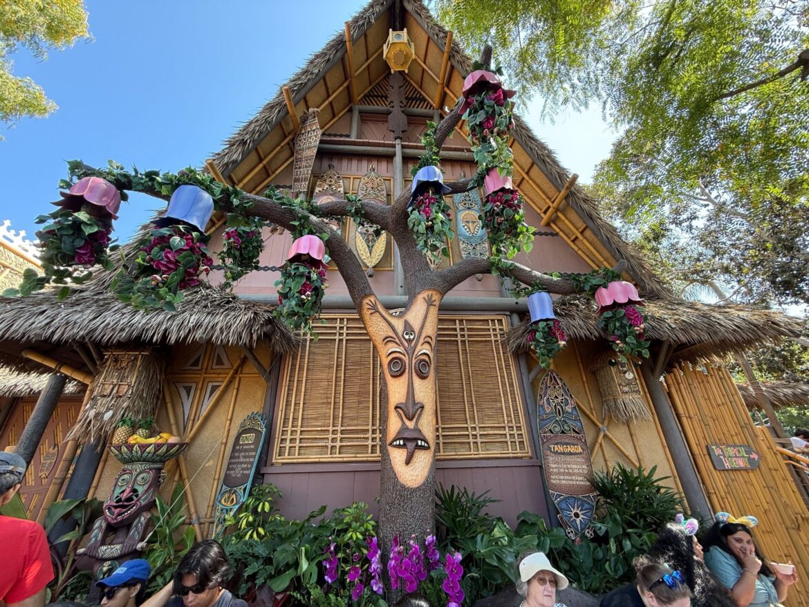 PHOTOS: Enchanted Tiki Garden Open to Guests Prior to July 3 Return of Walt Disney’s Enchanted Tiki Room Entrance sign for Walt Disney’s Enchanted Tiki Room in the Pre-Show Area, adorned with tropical carvings under a blue sky.
