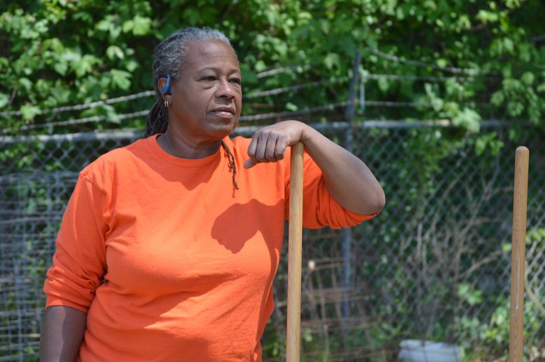 A woman in a bright orange shirt leans against a shovel outside