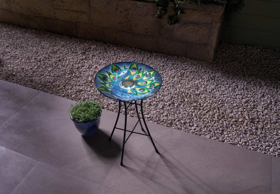 Solar-powered bird bath with peacock design.