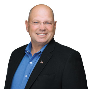 a headshot photo of pest expert Ed Dolshun: a smiling bald man in glasses looking at the camera wearing a true blue button up shirt under a black blazer