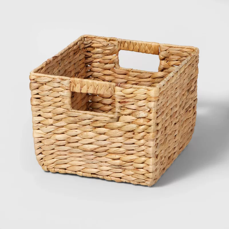 A small cube woven storage basket with cut-out handles.