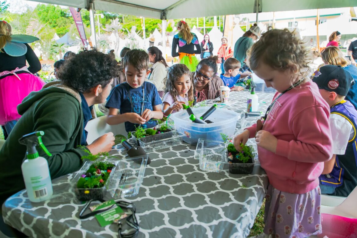 A parent/guardian with children at a table potting plants into a takeaway tray.