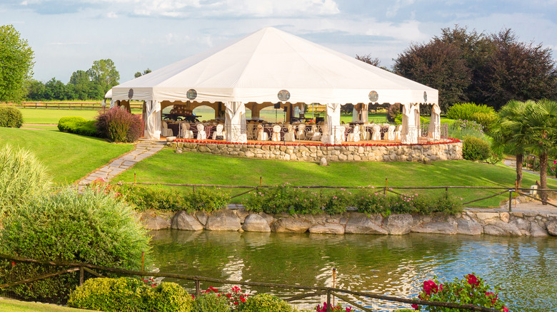 A white tent is set up in a spacious backyard near a pond