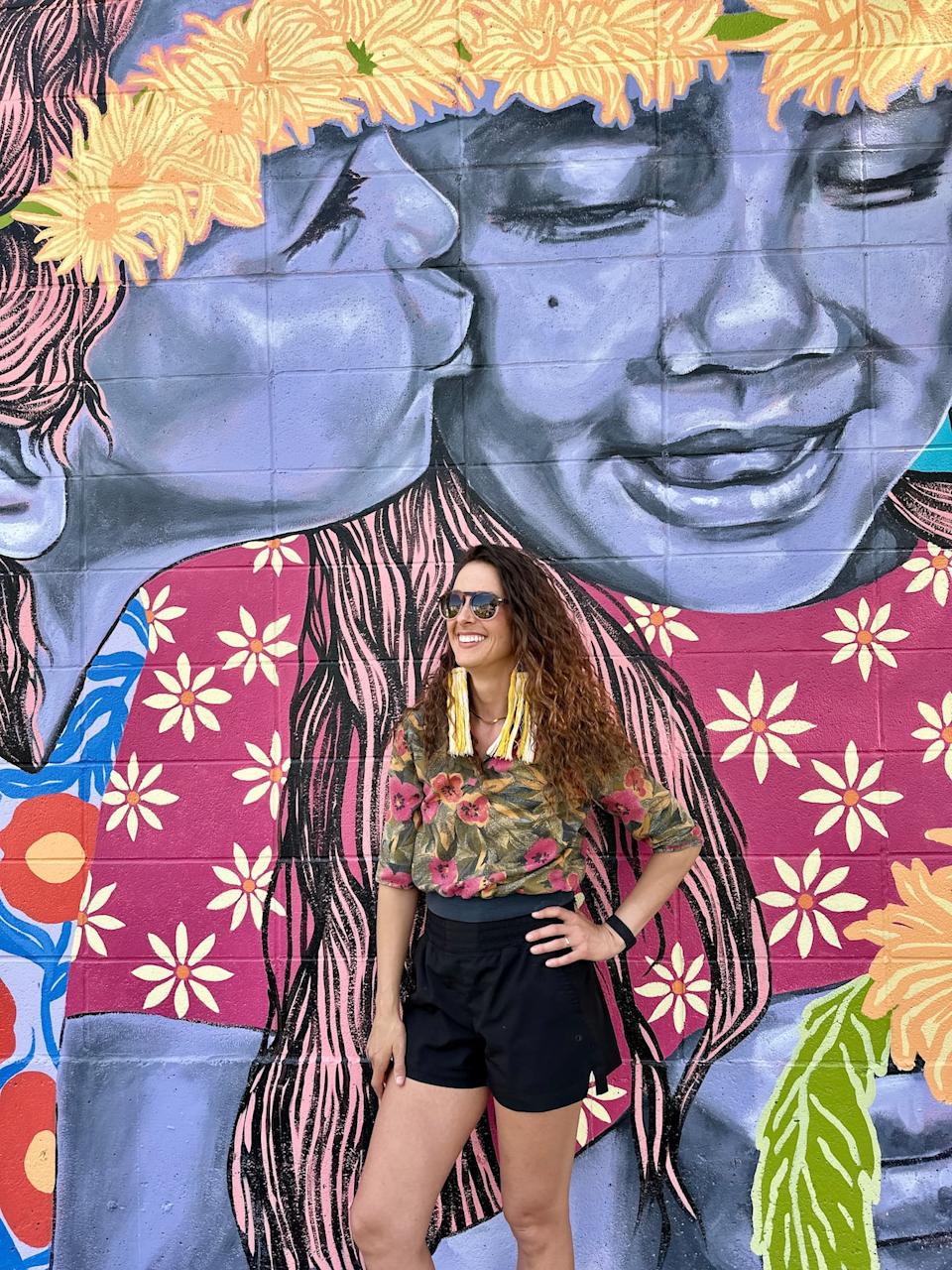 Artist Brandi Hofer stands next to her mural "Fairies in the Garden" at the Lloyd Public Garden at 49 St. 