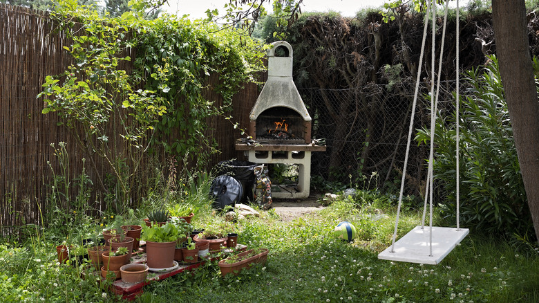 A tree swing hangs in a backyard near a lit fireplace and arrangement of terracotta pots