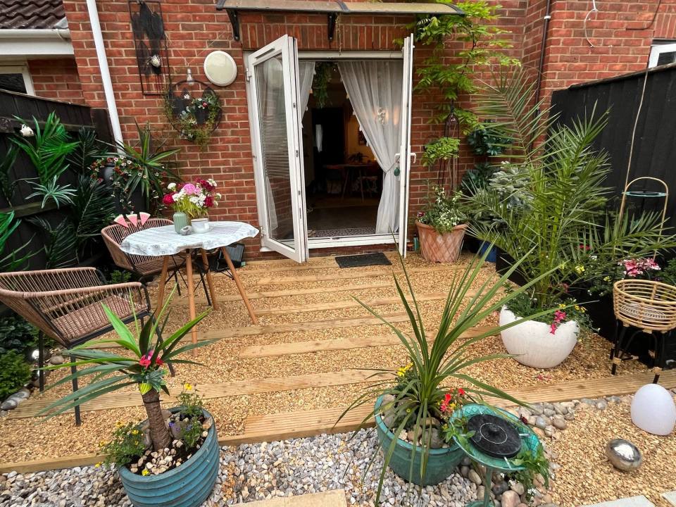 A patio garden with a wooden deck, potted plants, and outdoor furniture.