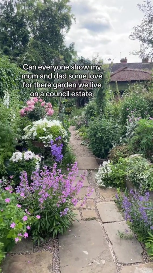 A stone path winds through a lush, flower-filled garden.