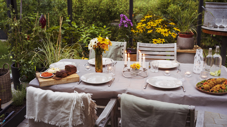 Taupe vintage linens cover a patio table surrounded by flowers