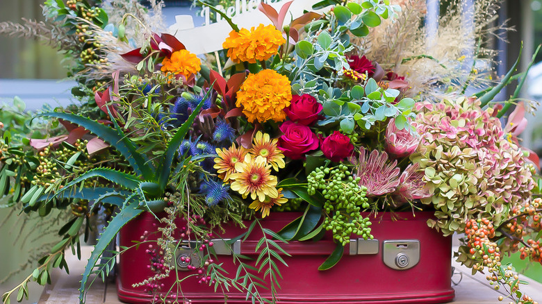A pink vintage suitcase is filled with colorful flowers