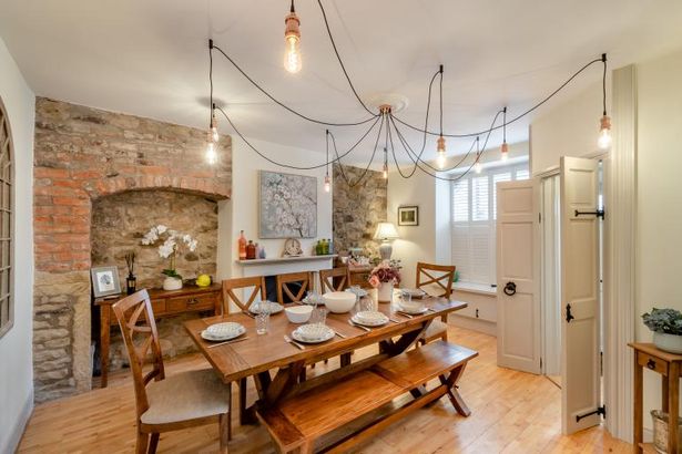 A wooden dining table in the centre of a room with wooden flooring and exposed brick wall.
