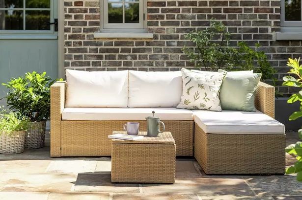 The 4 Seater Rattan Effect Garden Sofa Set set up on a flagstone patio outdoors in a garden.