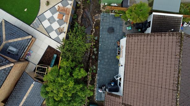 The image is a drone shot of the garden area with the flowing stream running beside it