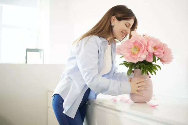 The woman arranges pink peonies in a vase in a white office.