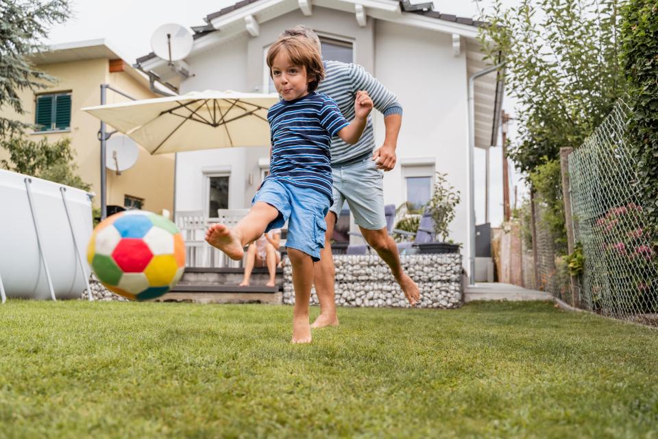 Father and son playing soccer in the backyard.
