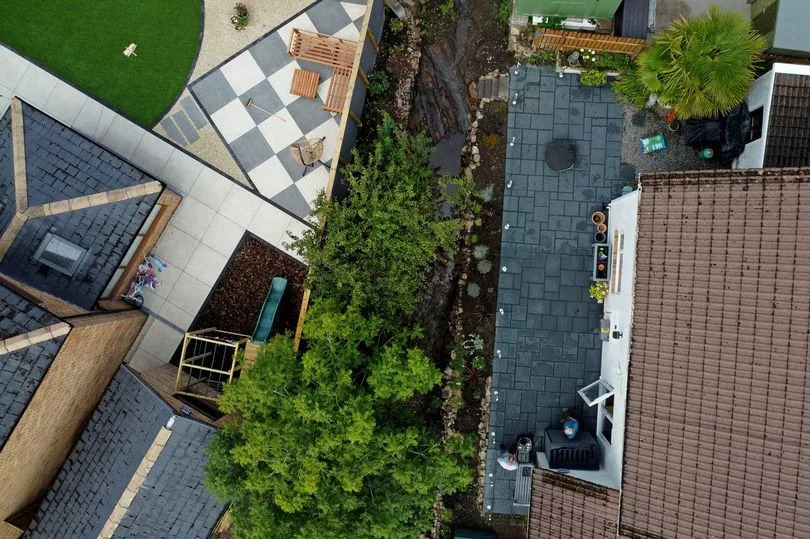 The image is a drone shot of the garden area with the flowing stream running beside it