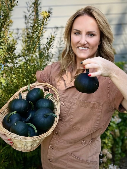 Woman in gardening outfit holding up a black pumpkin