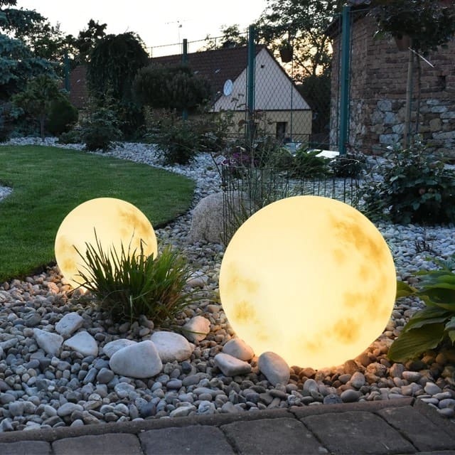 Two illuminated moon-shaped garden lights in a gravel garden.