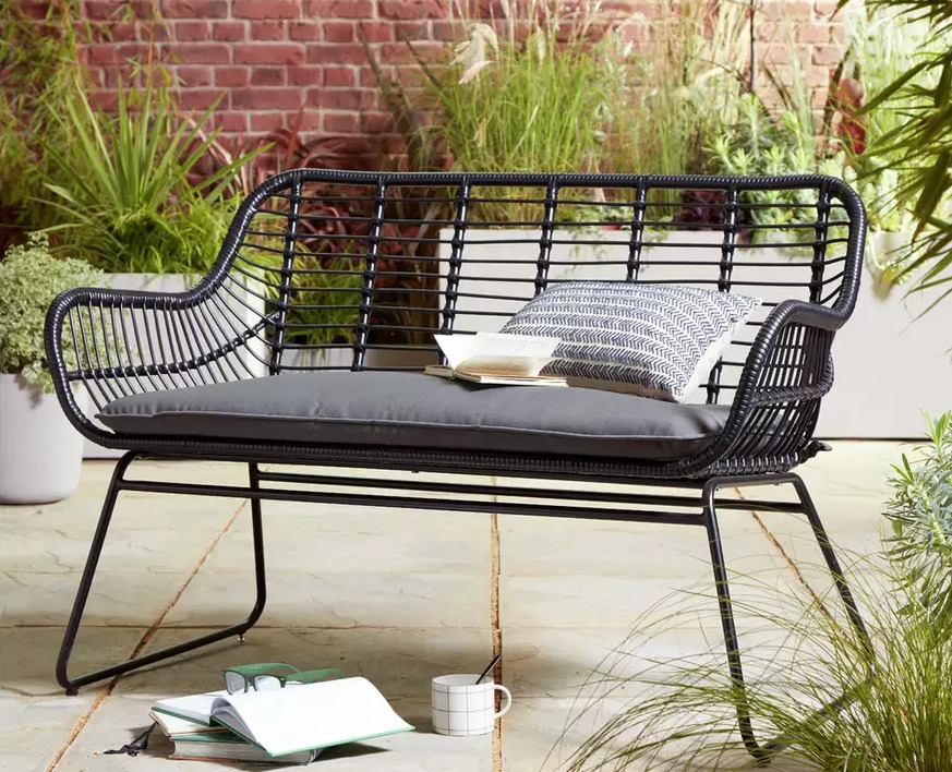 Black wicker patio bench with gray cushions.