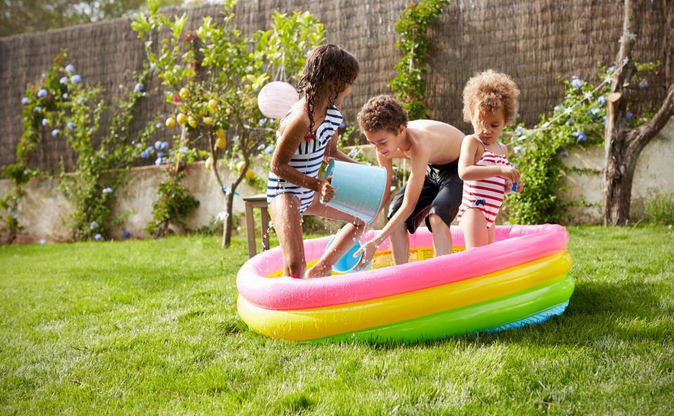 Three children playing in a paddling pool in a garden.