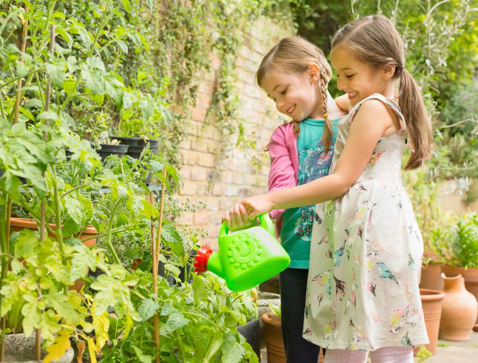 Two girls hugging while watering plants in a garden.
