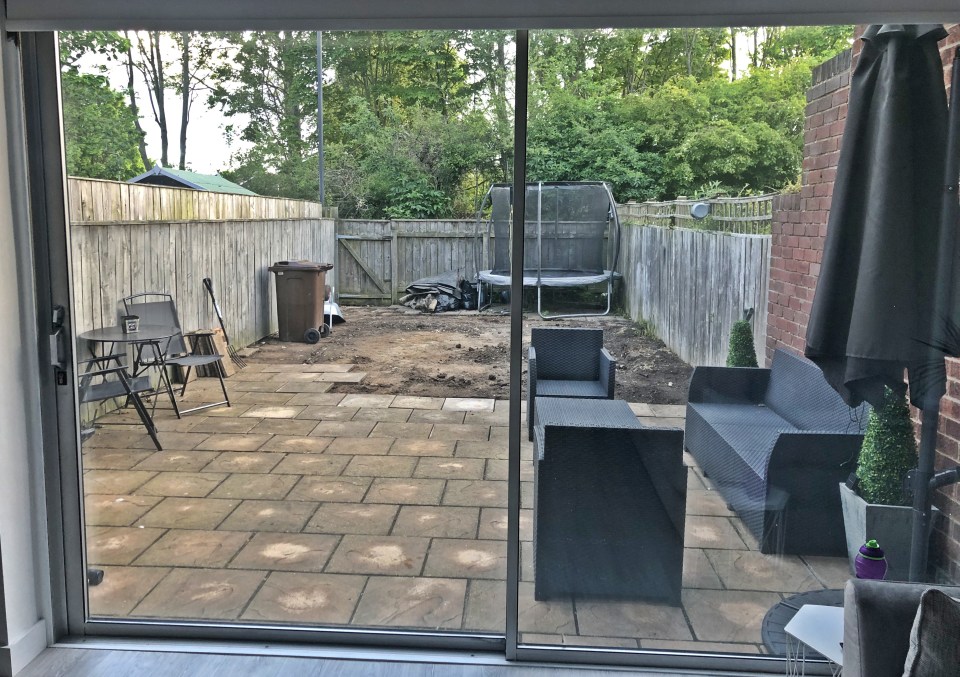 A view through a sliding glass door of a garden before renovation.