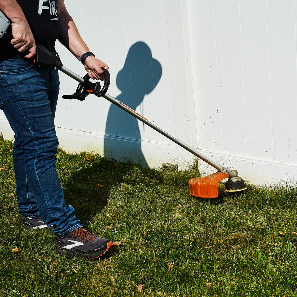 person using a weed trimmer near a white fence